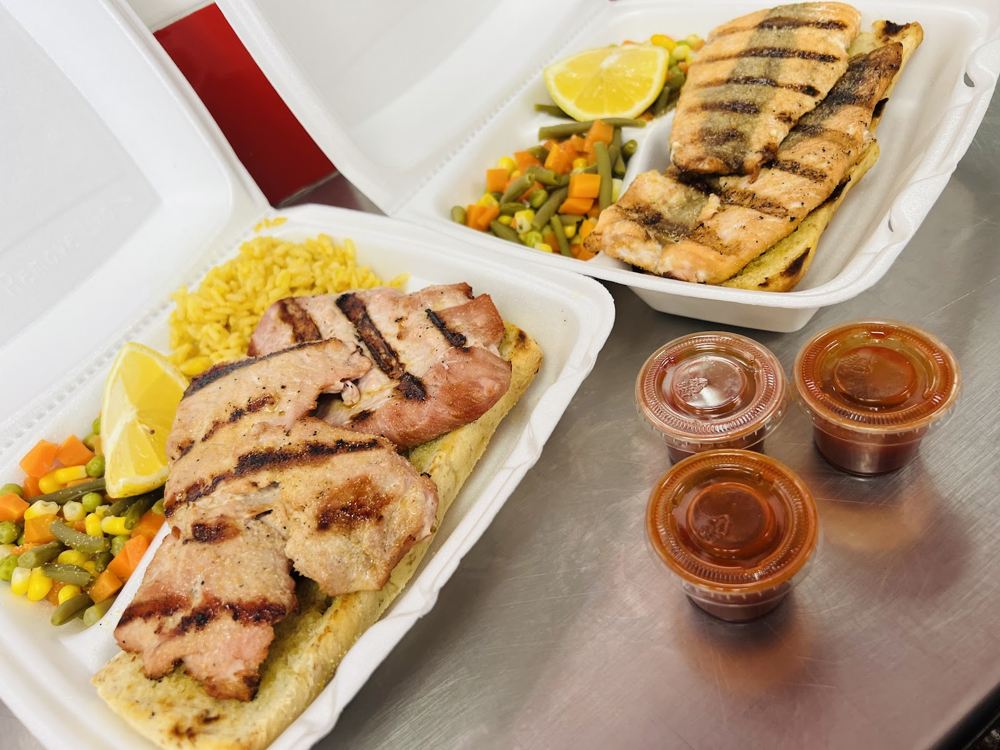 Two grilled fish dinners with vegetables, fries, lemon and sauces